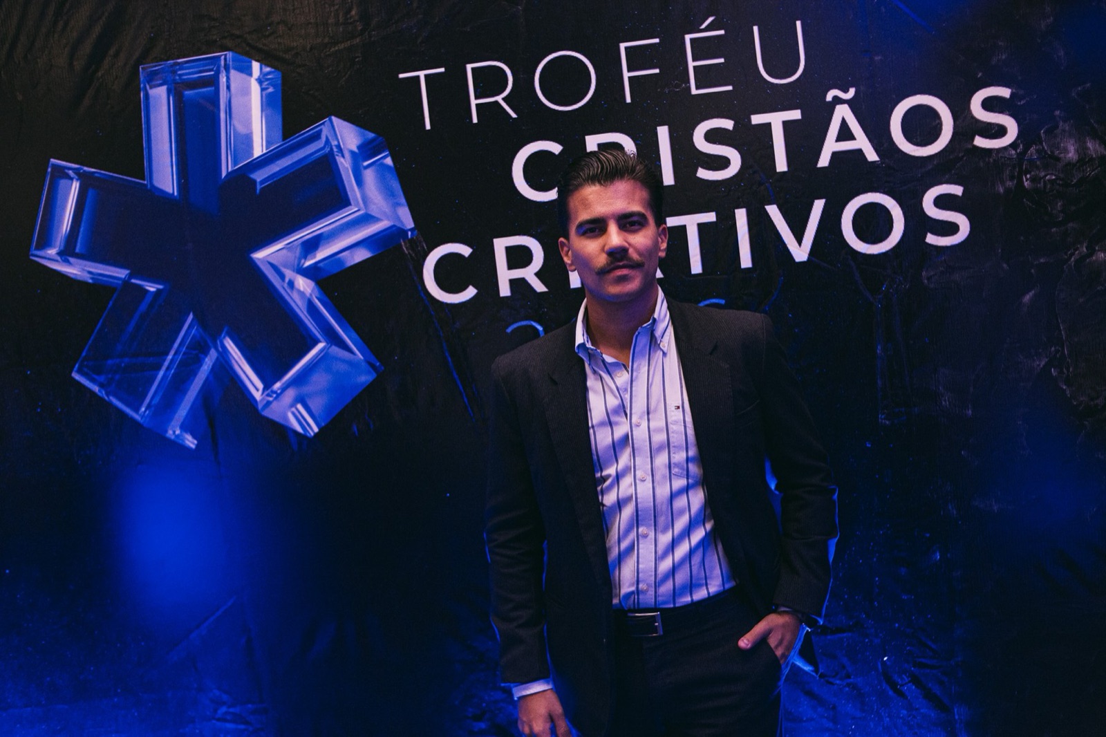 Victor Fortunato diante do painel do Troféu Cristãos Criativos 2026, com o símbolo de asterisco azul do prêmio